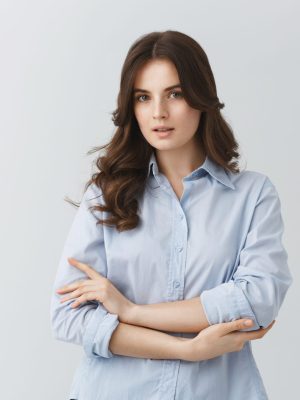 Tender beautiful young woman with dark wavy hair in blue shirt having serious look, posing for photo in article about young families